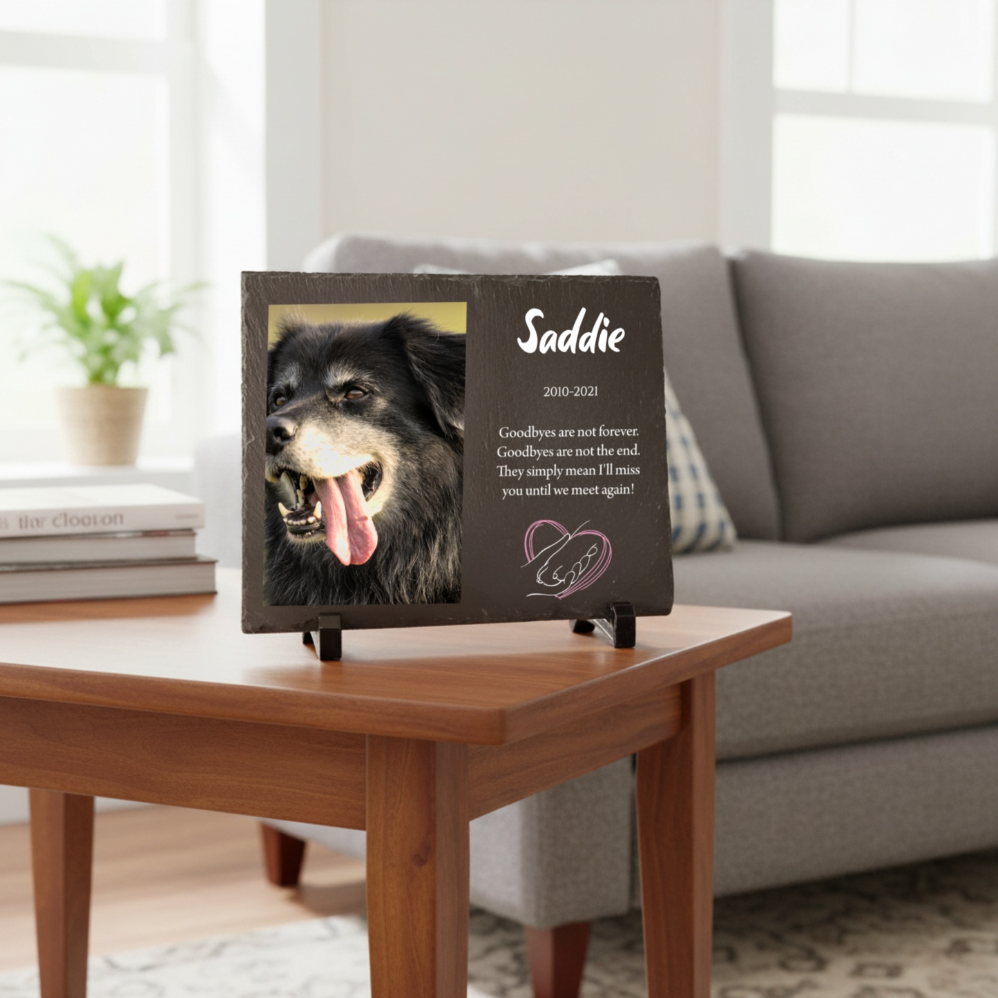 Dark slate memorial plaque printed with a photo of a dog named Saddie, the dates 2010 to 2021, a farewell message and a heart and paw design on a wooden table