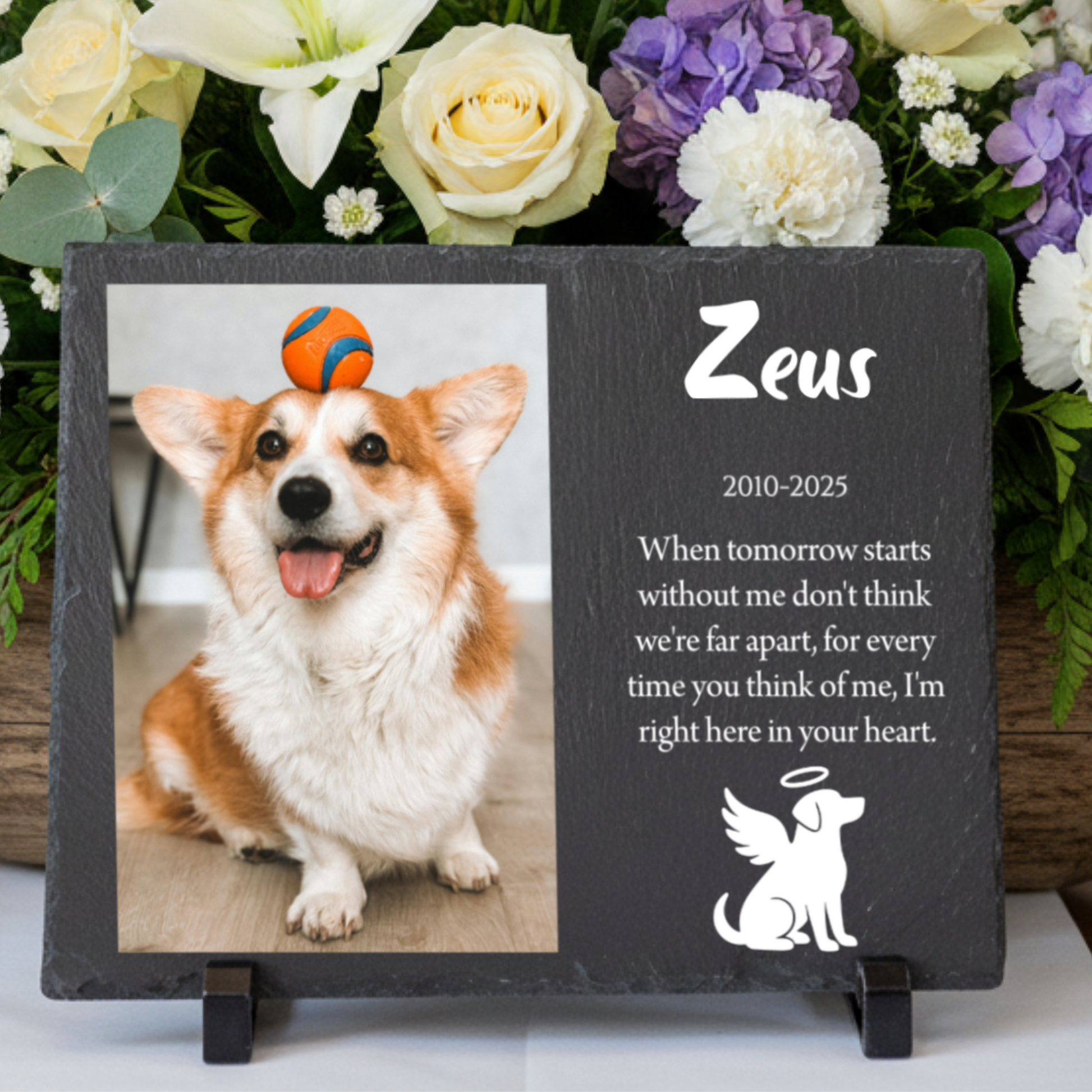 Slate pet memorial plaque printed with a corgi's photo, the name Zeus, the years 2010 to 2025, a personal message and a dog angel icon, on stands in front of flowers