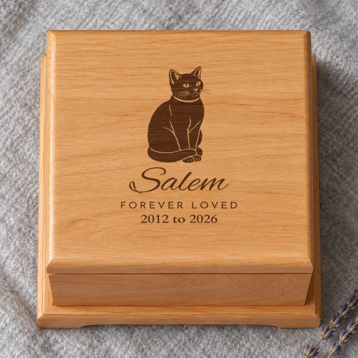 Lid of a personalized cat urn seen from above: a black cat drawing with Salem, Forever Loved and 2012 to 2026 laser engraved on red alder, on grey felt