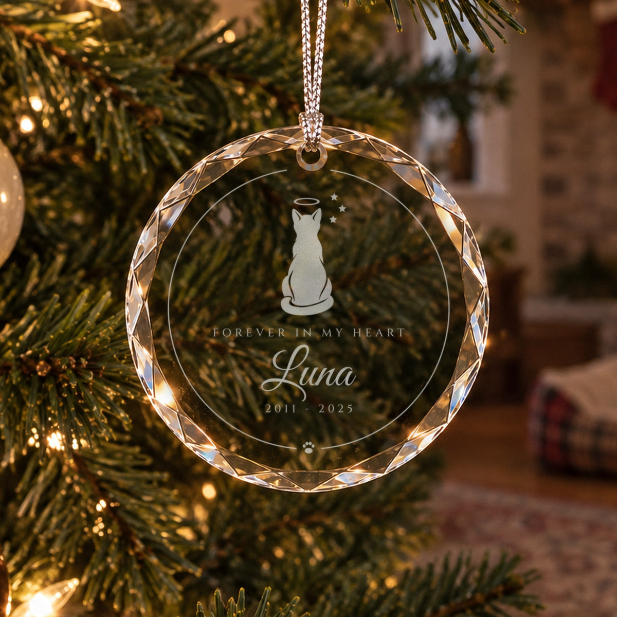 Personalized cat memorial ornament in faceted glass on a Christmas tree near an empty pet bed, engraved Forever in My Heart, Luna