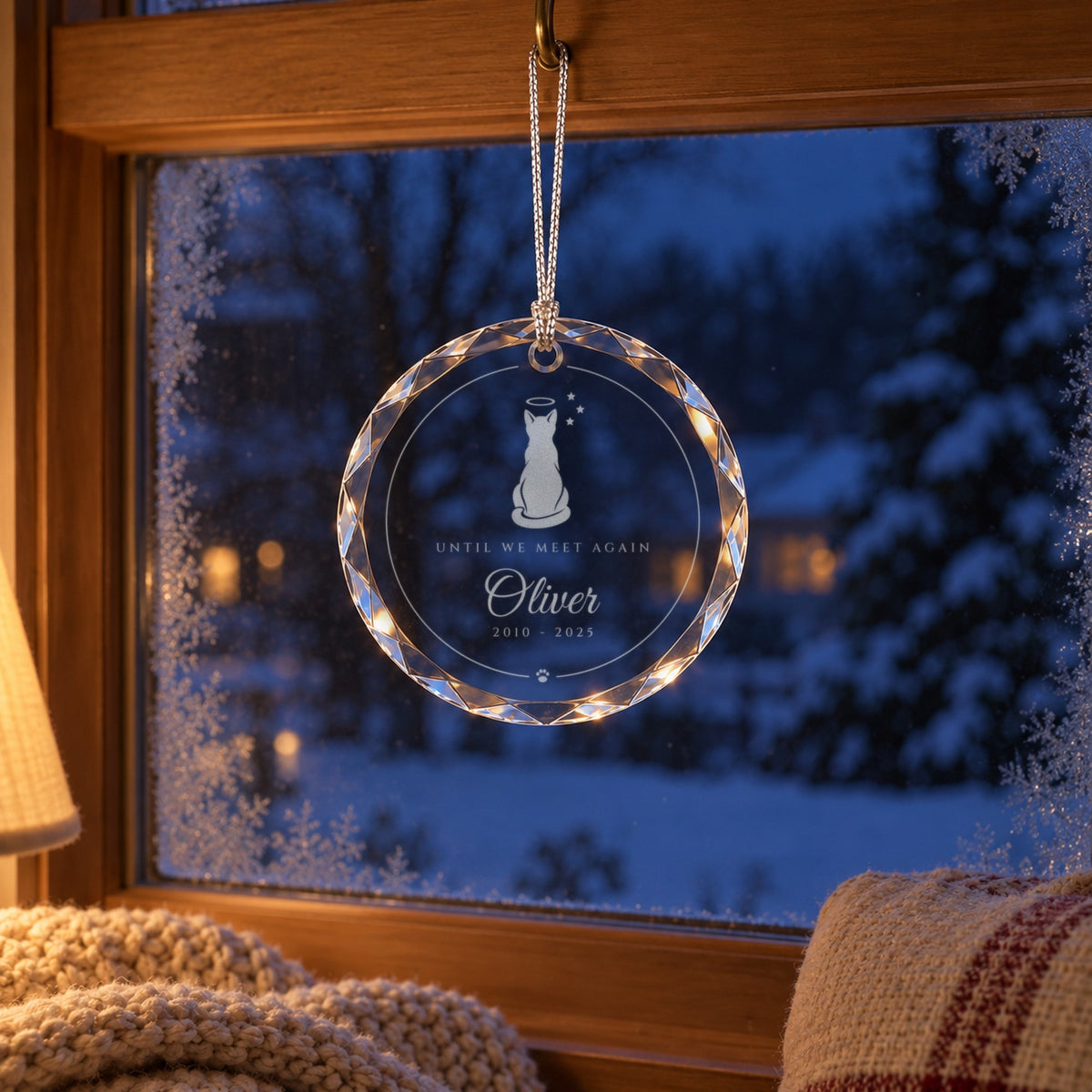 Cat memorial Christmas ornament hanging in a snowy window above a cozy window seat, engraved with a cat and a halo, Oliver
