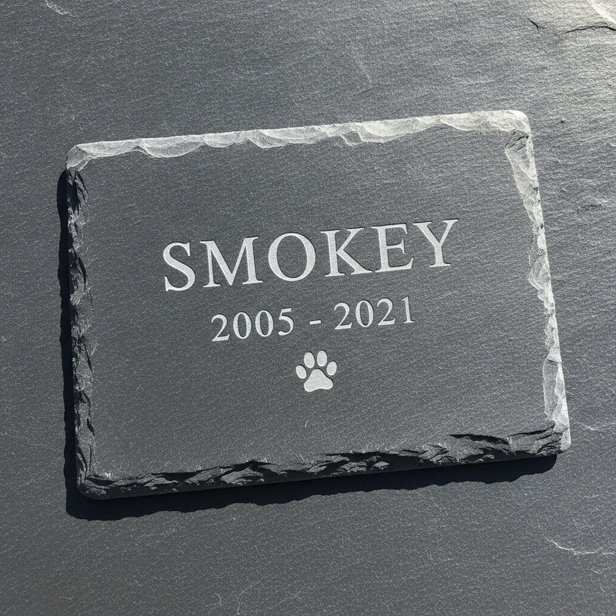 Close view of the recessed laser engraving on a natural slate pet grave marker, the sample name Smokey cut pale into the dark stone surface