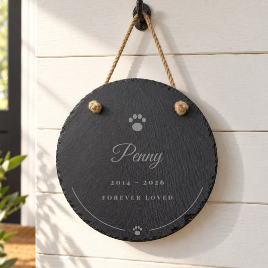 Hanging Pet Memorial Slate, a round engraved slate with a paw print, Penny, 2014 - 2026 and Forever Loved, hanging by a jute rope on a white shiplap wall