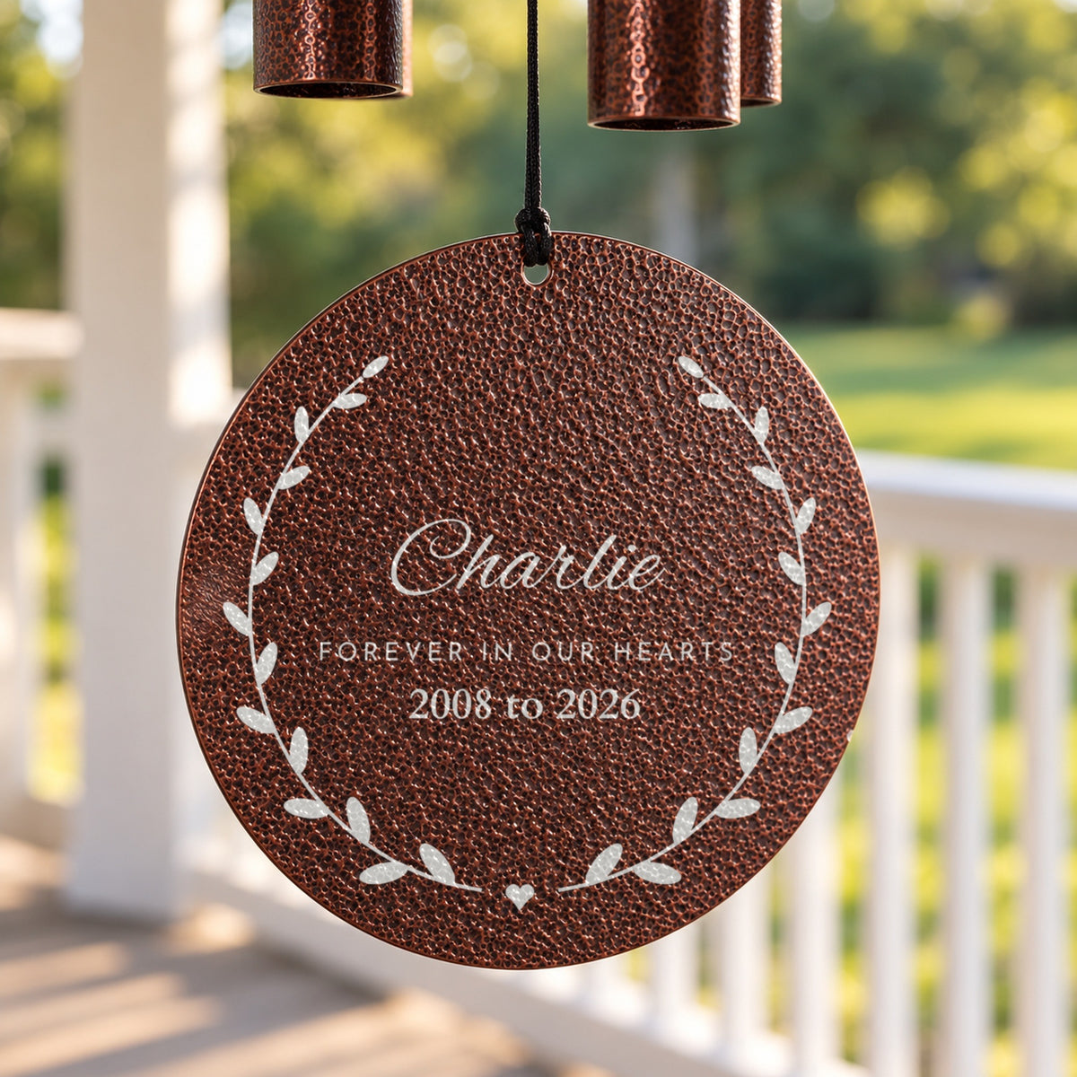 Close-up of the silver laser engraving on a copper memorial wind chime disc: the name Charlie, Forever in Our Hearts and 2008 to 2026 in a leaf wreath