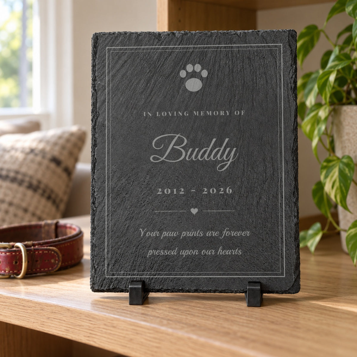 Paw Print Pet Memorial Slate engraved with a paw print, In Loving Memory Of, Buddy and 2012 - 2026, standing on an oak shelf beside a worn red dog collar