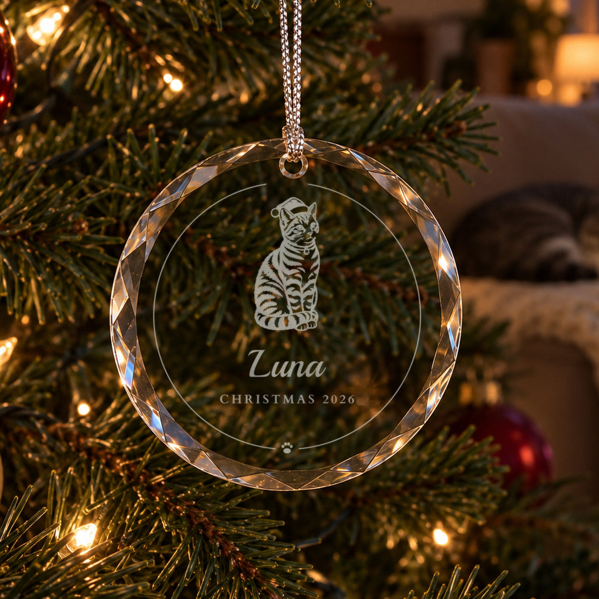 Personalized cat Christmas ornament in clear faceted glass on a lit tree, engraved with a tabby cat in a Santa hat, Luna and Christmas 2026