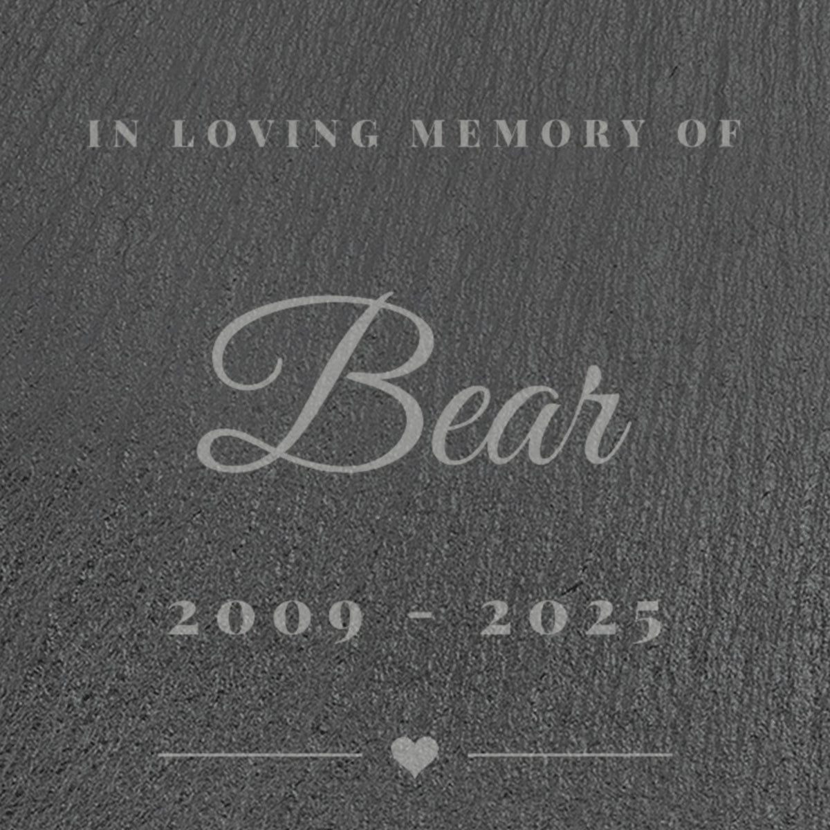 Close-up of the laser engraving on the pet memorial slate: In Loving Memory Of, Bear in script and 2009 - 2025 in pale grey on dark slate